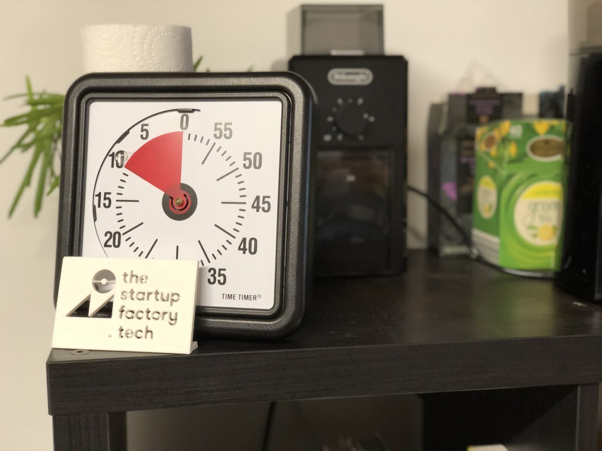 Picture of a time timer device on top of a shelf, with a 3D printed logo in front and blurred out hot drink facilities behind.